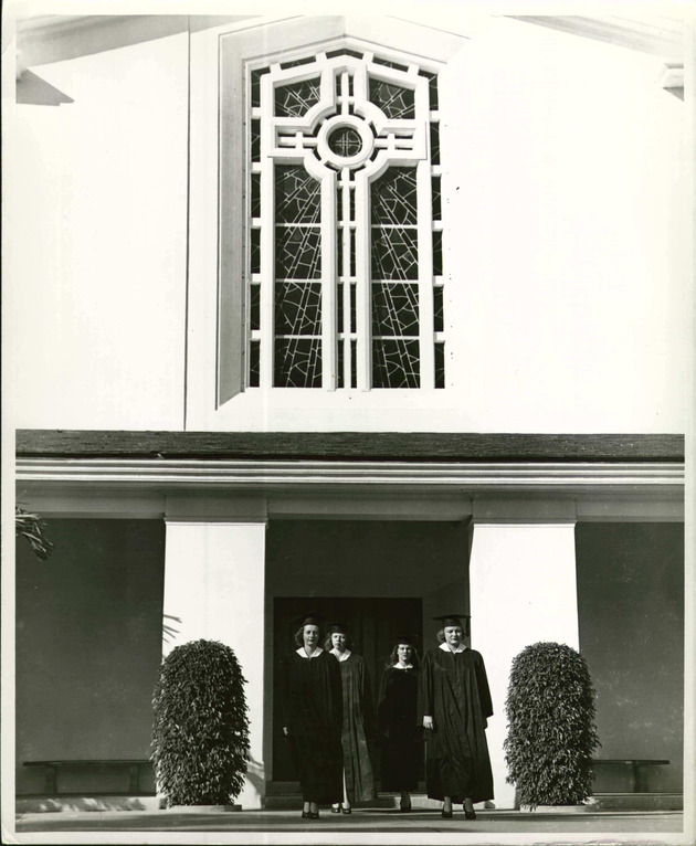 Four students wearing their academic formal attire leave Cor Jesu Chapel